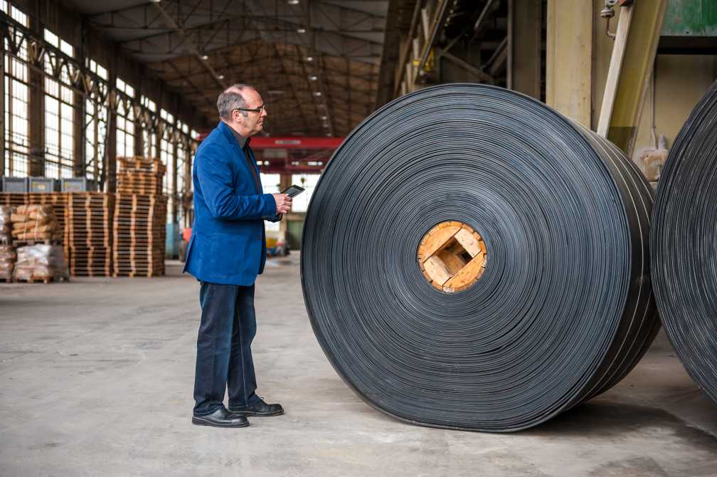 Manager with digital tablet in factory hall with rolls of rubber